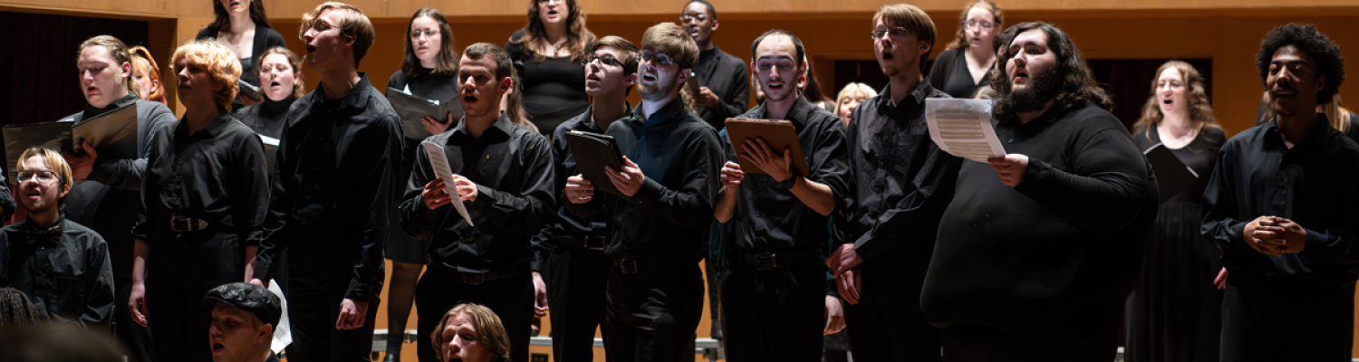 A group of choral singers wearing all black performs on stage
