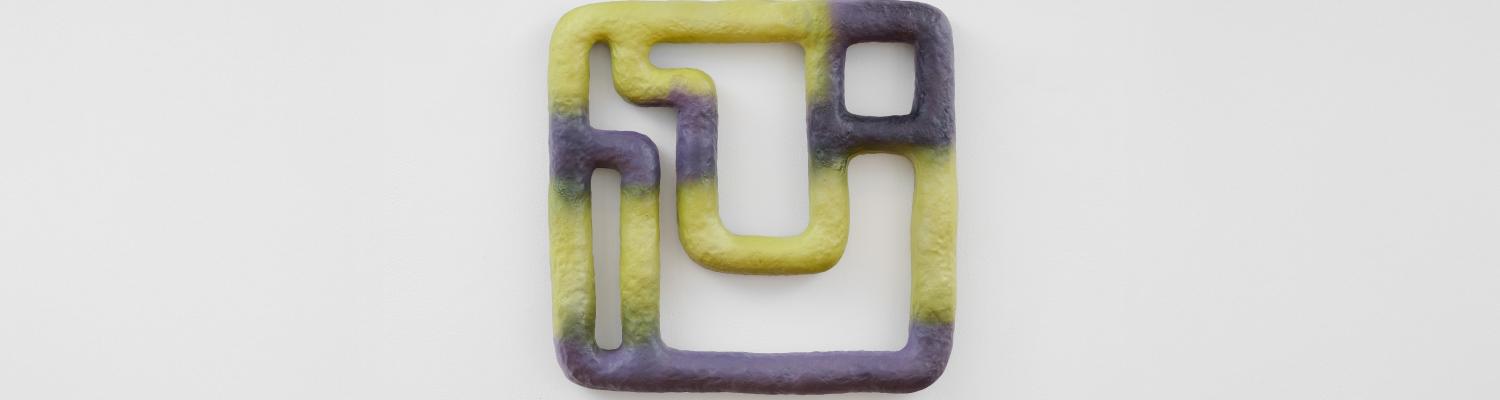a purple and green geometric sculpture hanging on a gallery wall