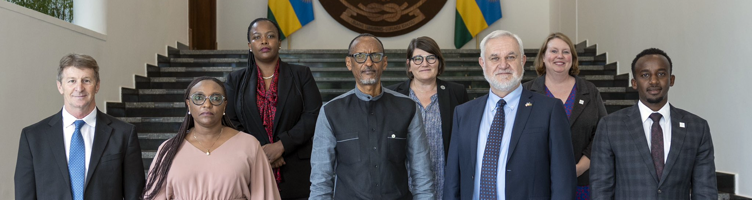 Rwandan President Paul Kagame stands at center with a delegation of eight people posed on the steps inside the Office of the President in Kigali, Rwanda. Two Rwandan flags and an official government seal are visible in the background.