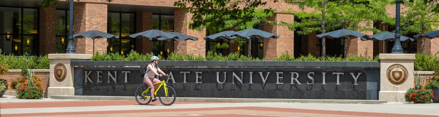 A cyclist riding past the �Ը������� University fountain on a sunny day.