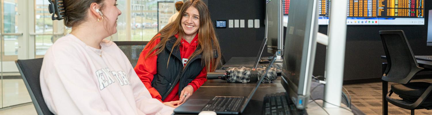 students working on computers and laughing in the finance trading floor classroom. 