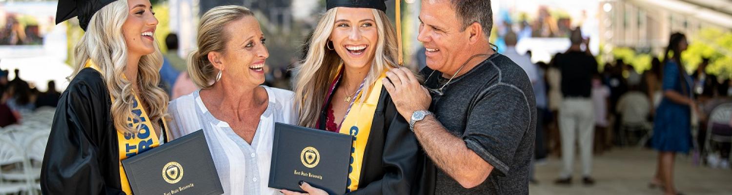 Two graduates hold their diplomas and celebrate with their parents.
