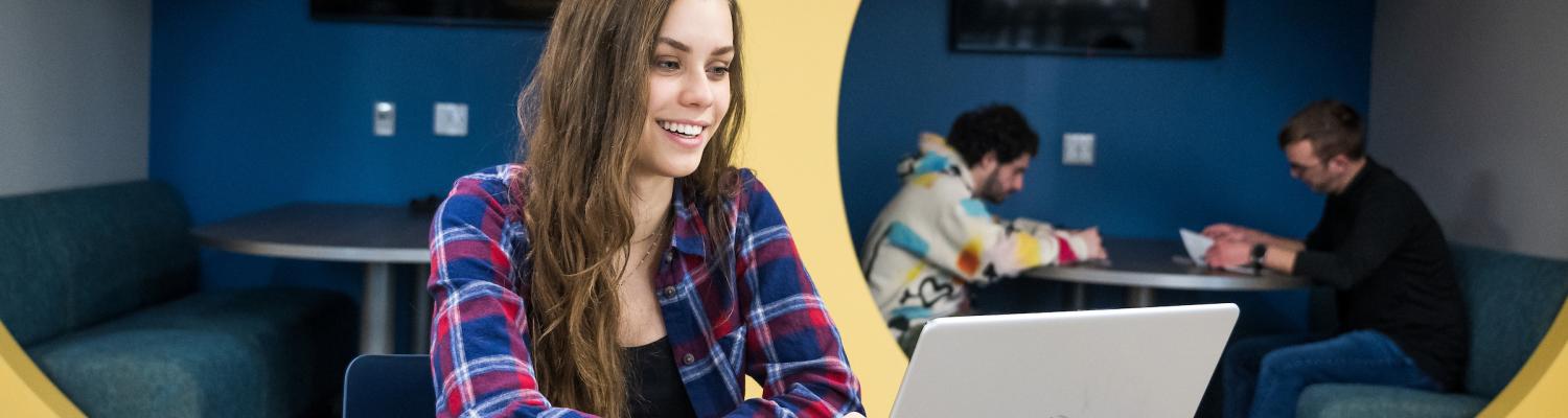 A female student smiling at her laptop with notebooks open beside her