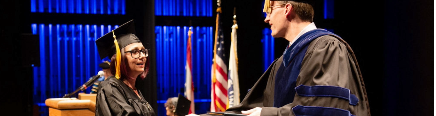 Student walking across stage to receive her diploma from Dean Bill Ayres, Ph.D.