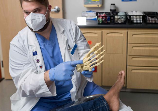 Student in medical gear pointing to a skeletal figure of a foot