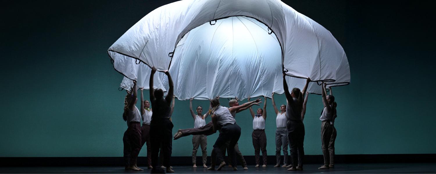 Dancers lift a dancer while the other dancers hold a parachute in the air