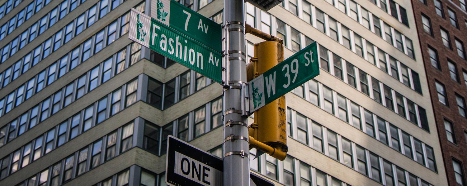 Street signs point various directions at an intersection with a towering cityscape building in the background