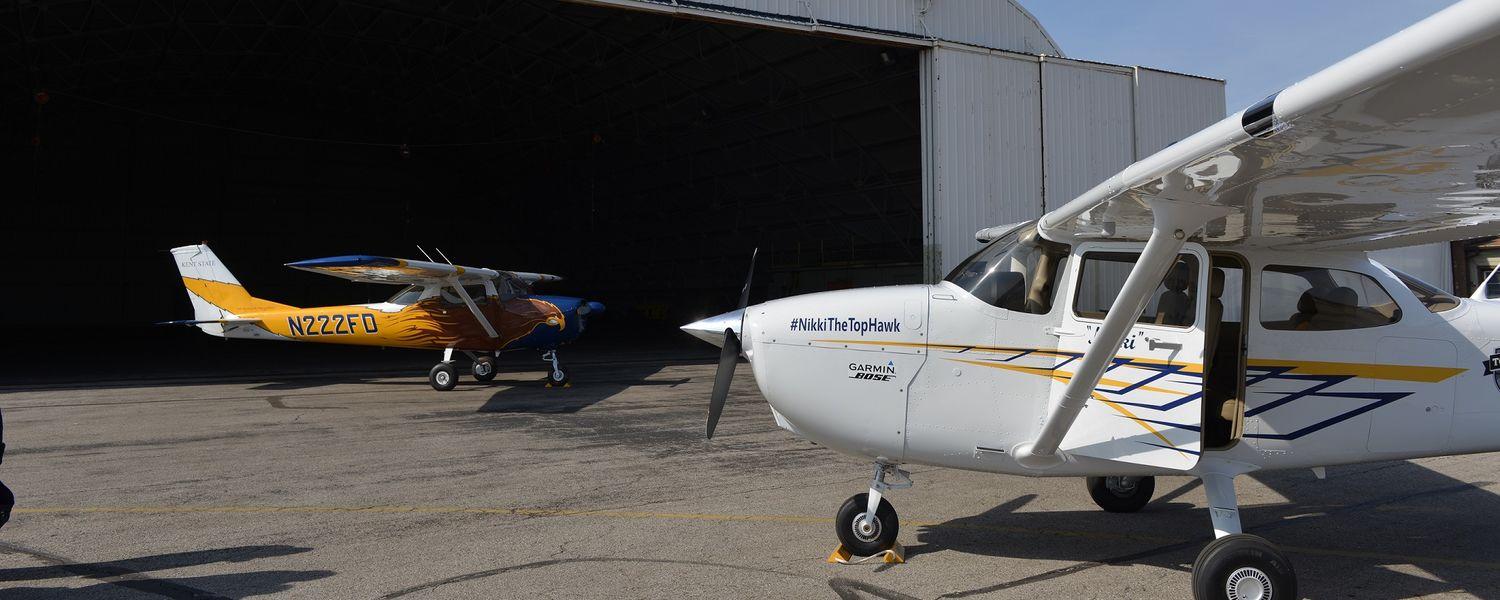 Two airplanes parked outside the Kenty State Airport Hangar.