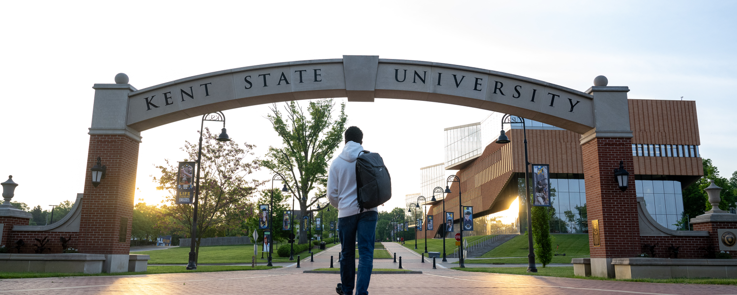 A student walks under the Kent State arch at sunrise.