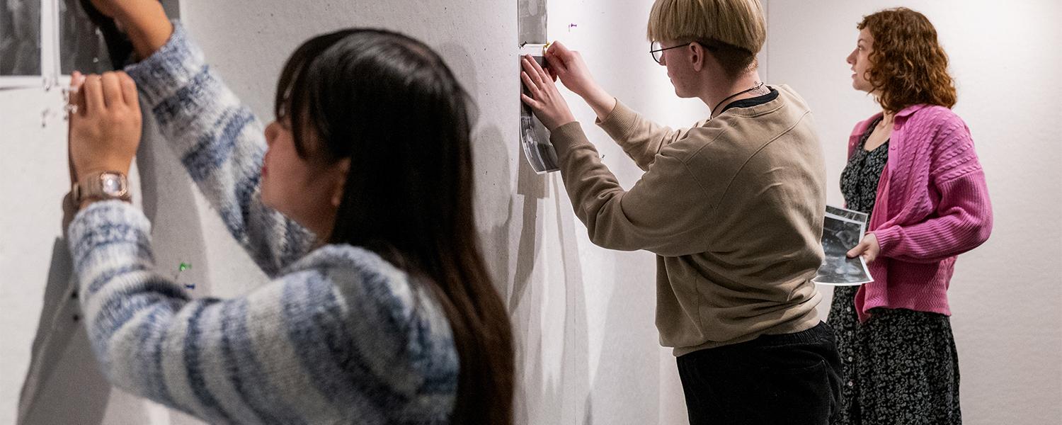 students hanging photos on wall for critique