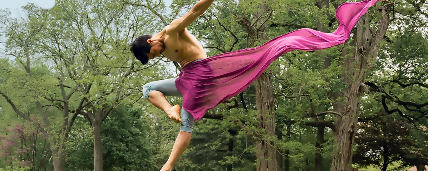 Male dancer leaping outside with a pink scarf