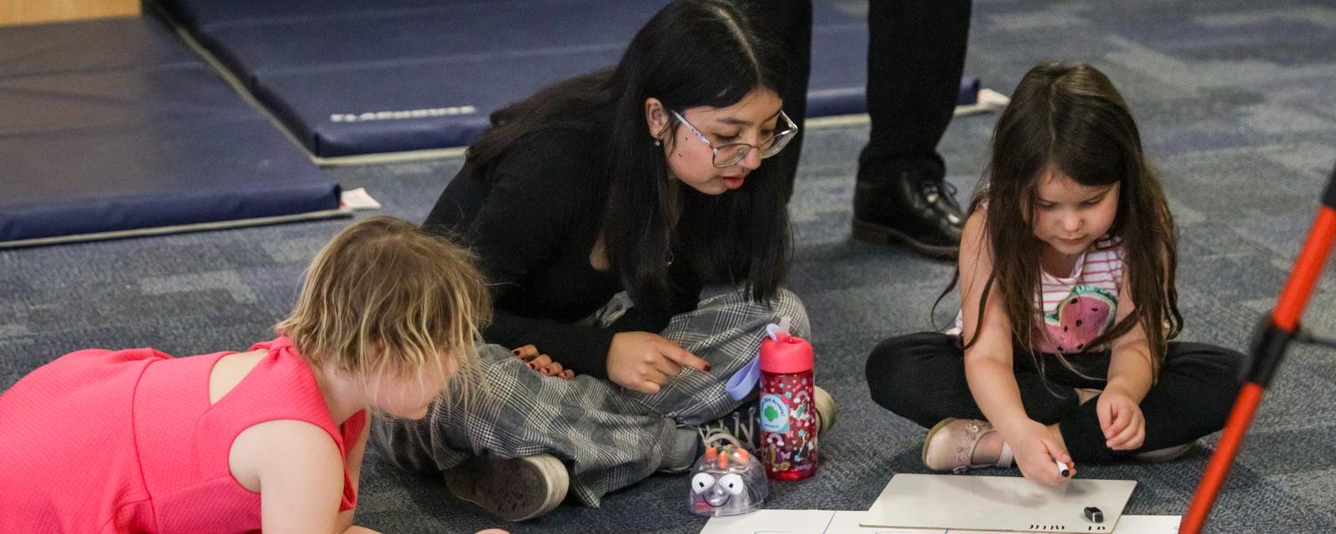 A student working with children in the Child Development Center with coding robots.