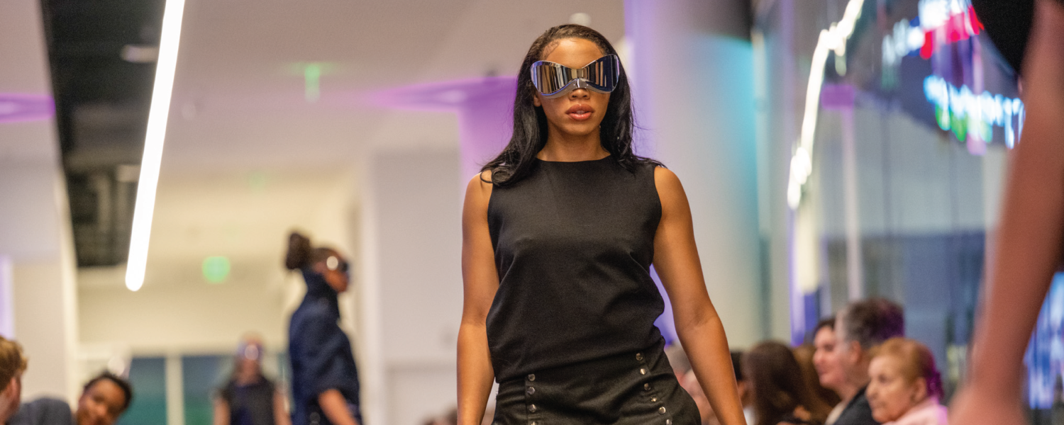 A model walks down the runway with black glasses and a black, sleeveless garment