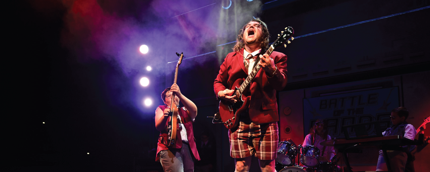 Lead singer of school of rock dressed in school uniform plays red electric guitar while singing