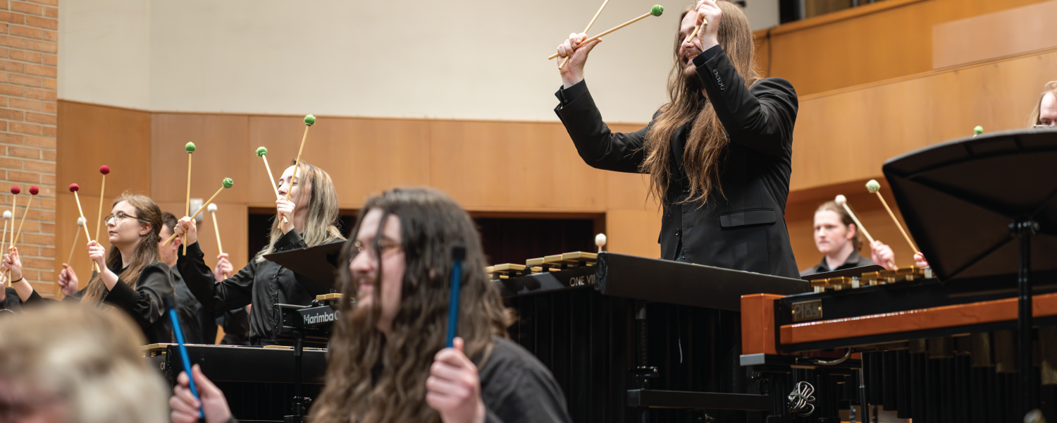 Percussionists raise their mallets with both hands while smiling