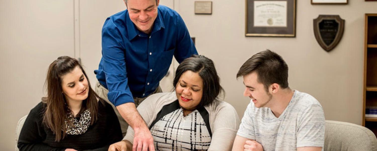 Professor points to book for a group of three students. 