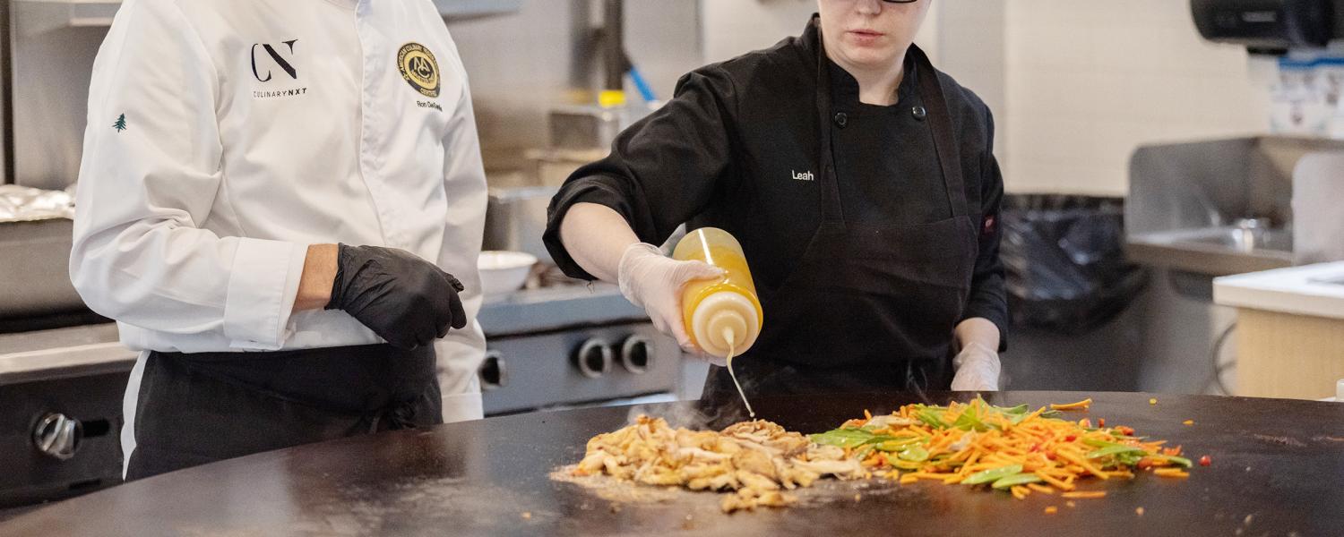 Certified Master Chef Ron DeSantis with a University Culinary Services team member seasoning raw chicken. They prepare a meal together in one of the new microconcepts at DI Dining.