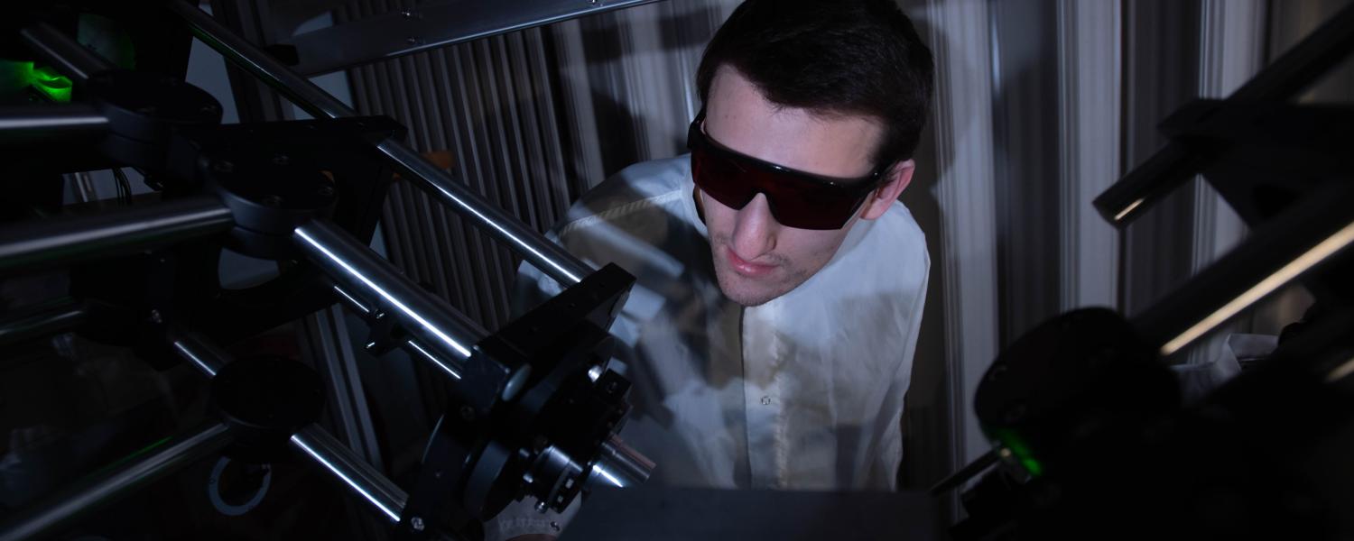 A male student with dark glasses inside a laboratory examining the equipment