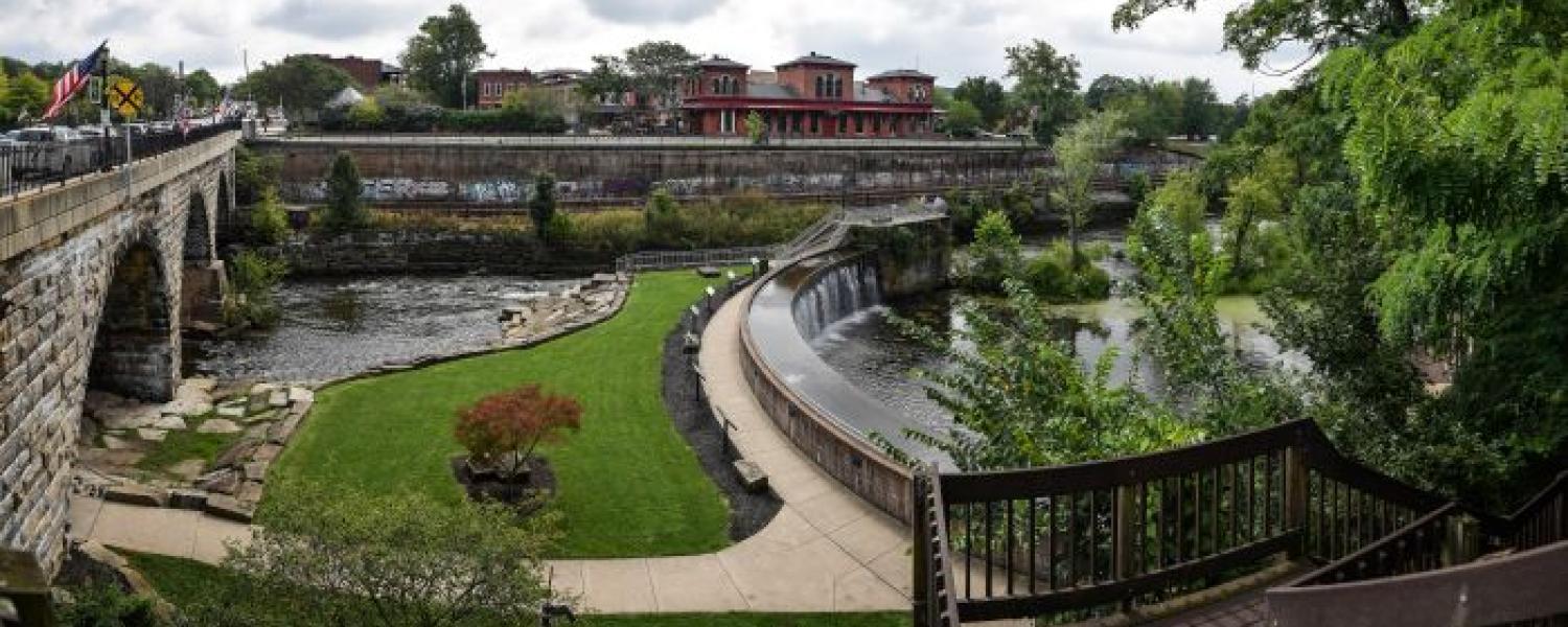 Scenic photo of the downtown Kent, Ohio waterfall flowing over rocks with surrounding greenery.