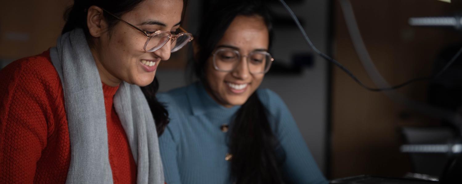 An image of 2 female students inside a dark lab, conducting research.