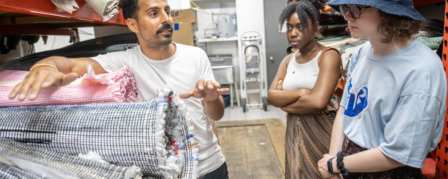 Alex talks to students as he leans against rolled sets of fabric