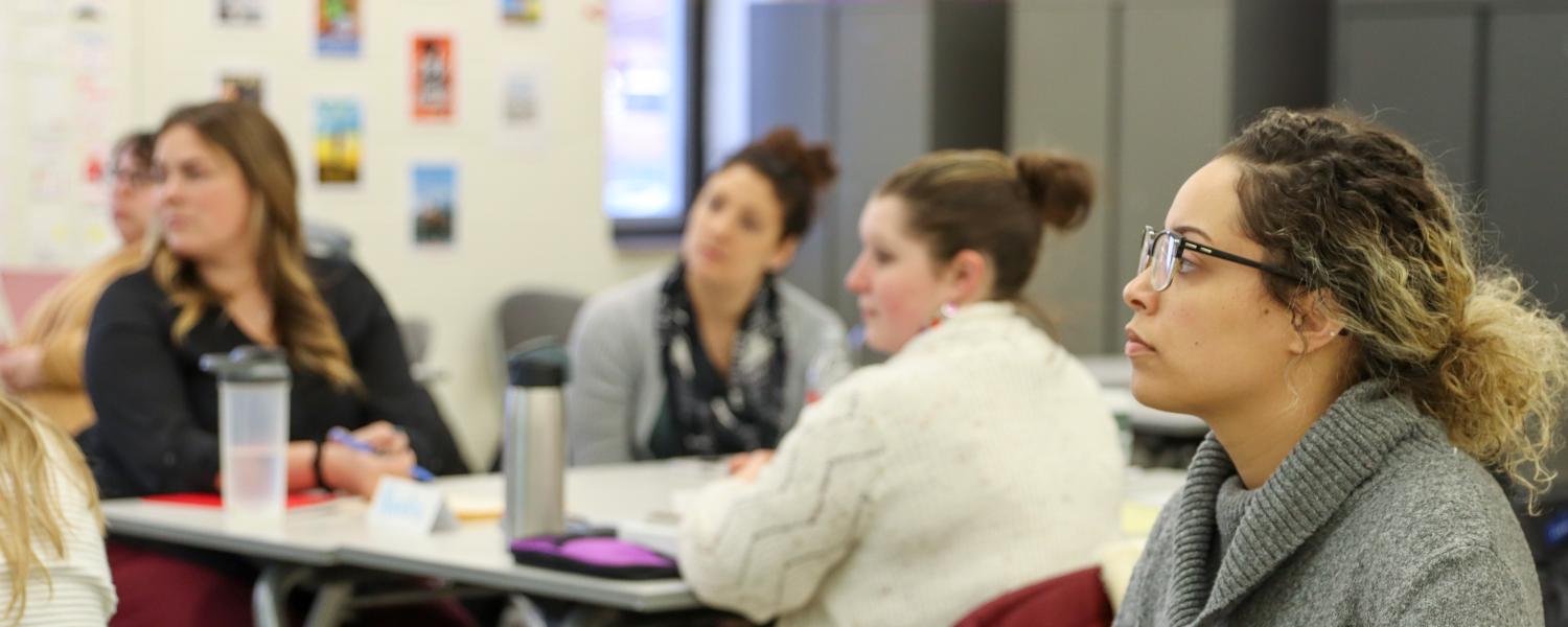 A classroom of Master's students listening to an instructor.