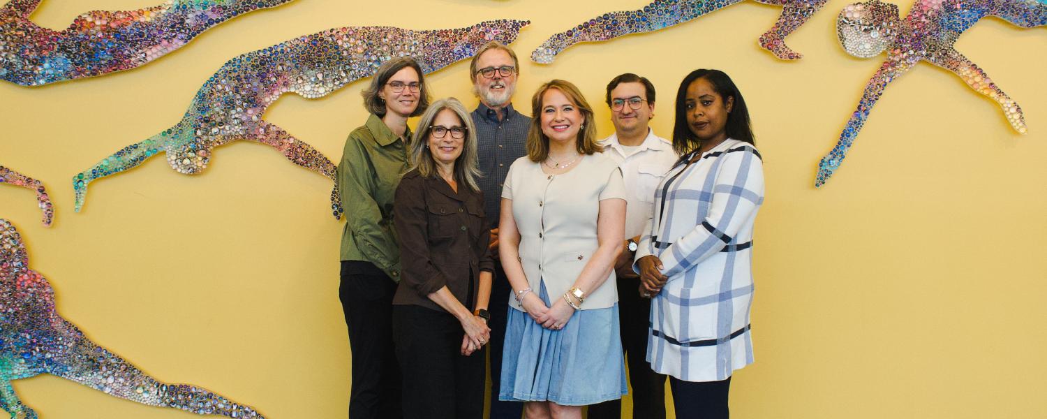 Group of people standing in front of a yellow wall with artwork behind. 