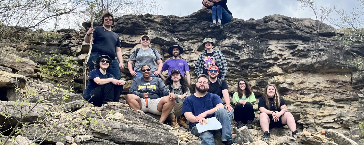 A group of students poses for the camera while standing and sitting on a large rock formation.
