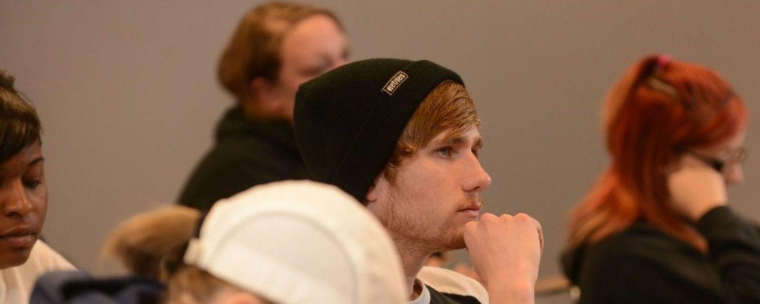A student sits in class with their hand under their chin, listening thoughtfully during a lecture.