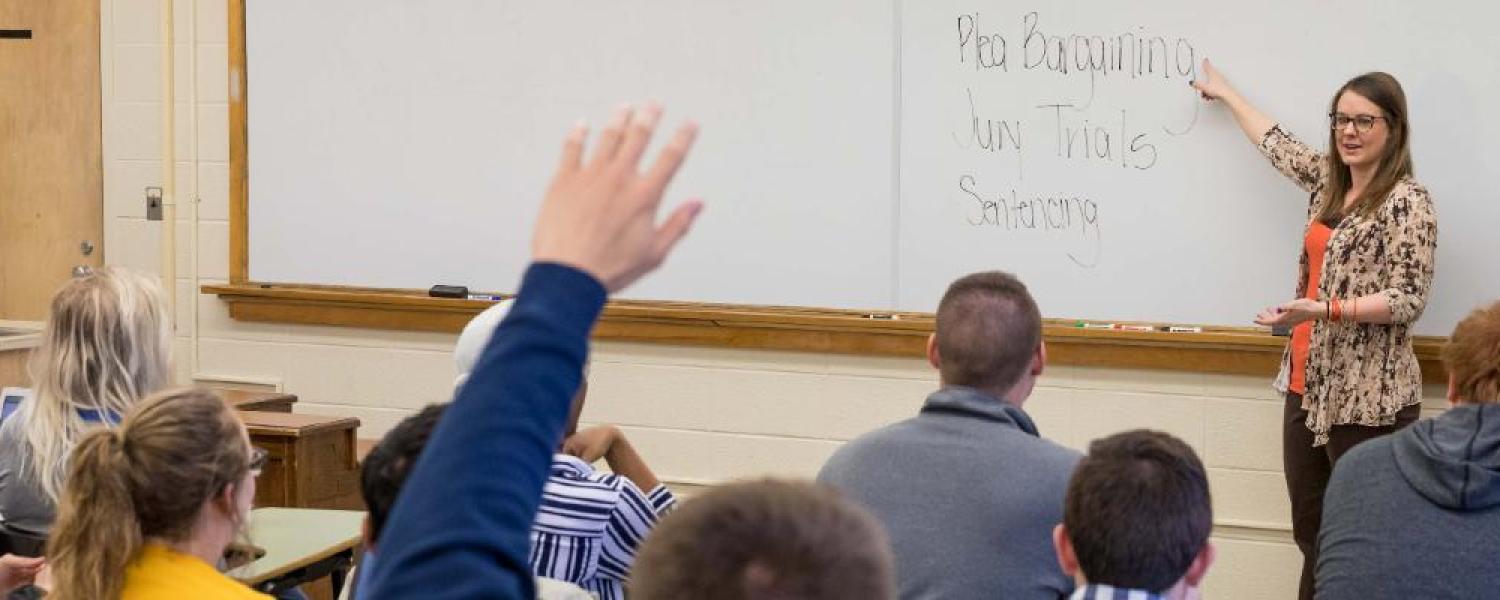 Students in a classroom raise their hands during a lecture.