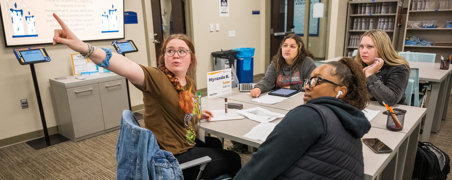 Three students sit at a table in the Academic Success Center with a tutor.