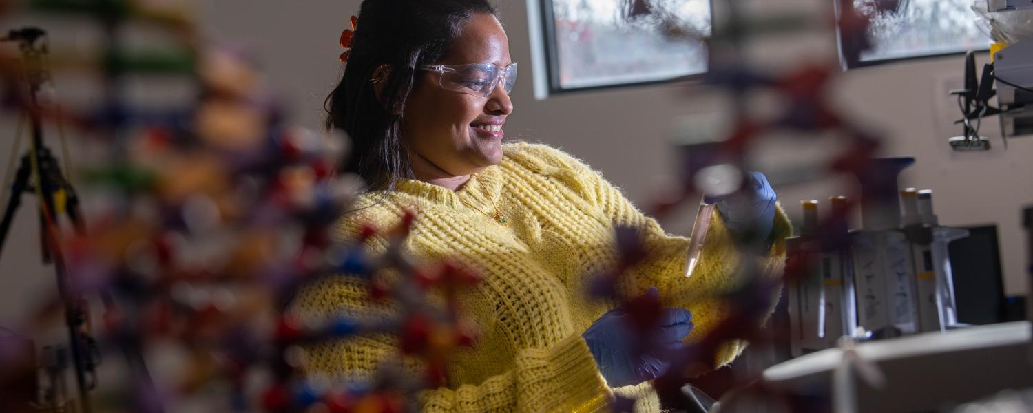 An image of a female student wearing yellow lab coat conducting research.