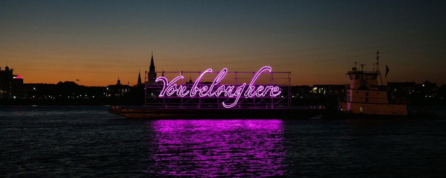 Large art installation of a neon sign that says "You Belong Here" on a body of water.