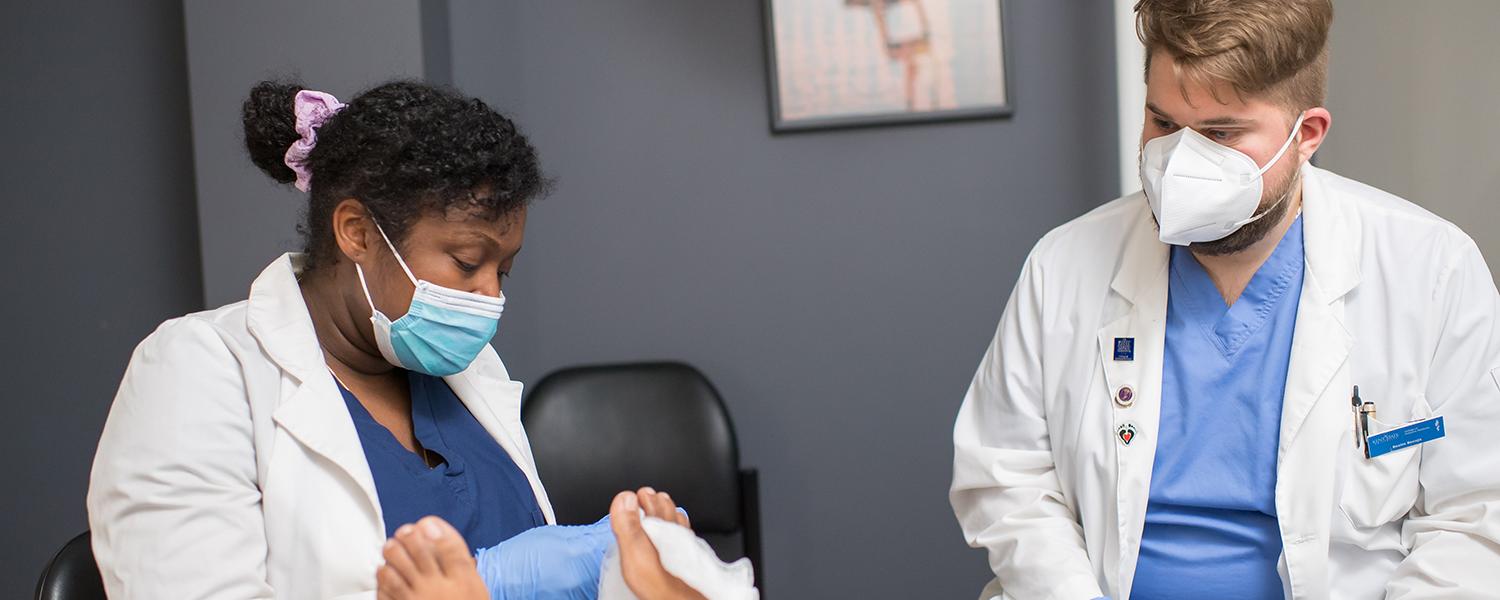 Two podiatry students with masks on inspecting a patient's foot.