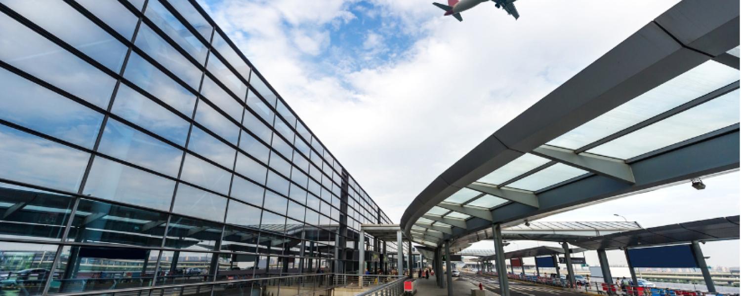 Photo of airport with plane flying in sky above.