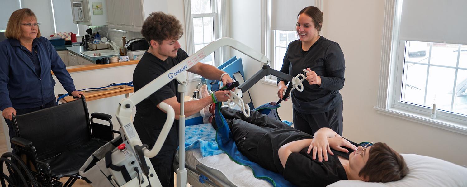 One male and one female OTA student assist another student in a bed