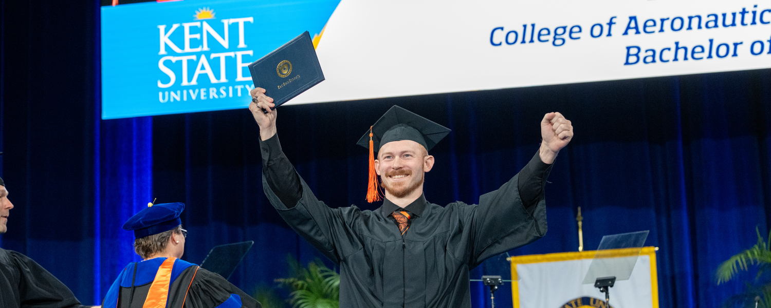 A student celebrates on stage at commencement with their degree in hand.