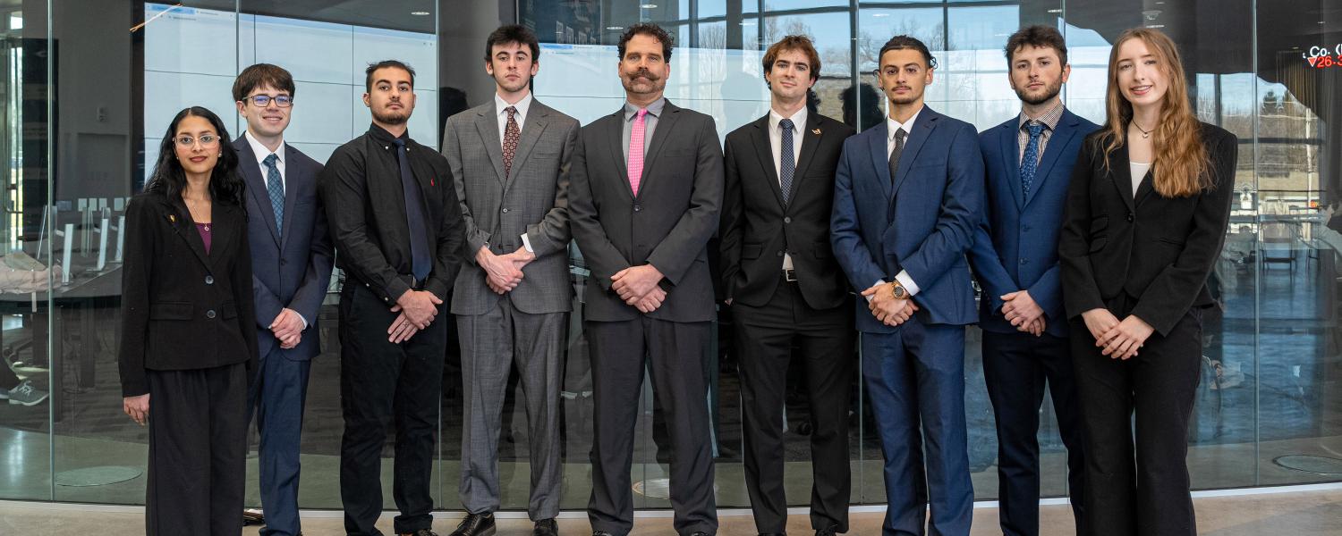 The finalists for the 2026 competition standing in business suits in front of the finance lab.