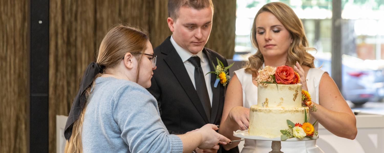 Brooklyn Fockler Leshon assists the bride and groom in staging the cutting of the wedding cake. 