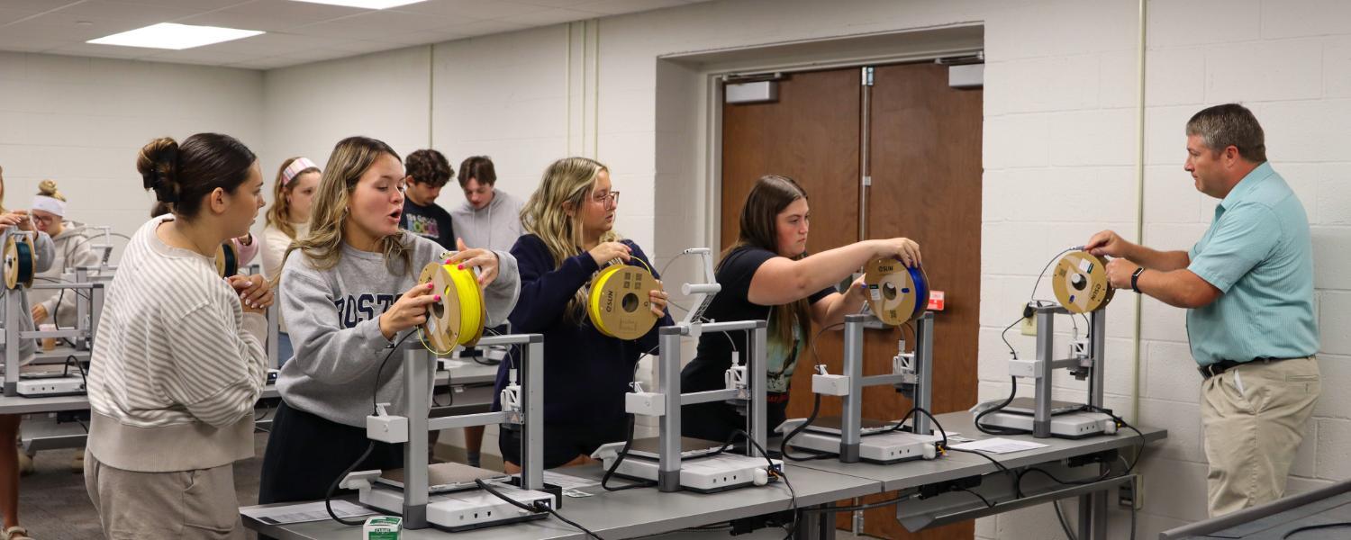 Students loading 3D printing filament onto the printers