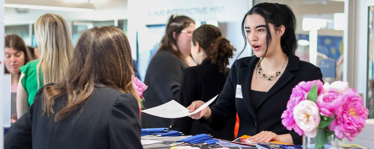 A student handing an employer a resume during a career fair. 