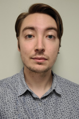 A headshot of Andrew Summers wearing a patterned gray button-up shirt against a plain background.