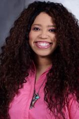 A long curly haired woman with brown skin, dark auburn hair, and a bright pink shirt