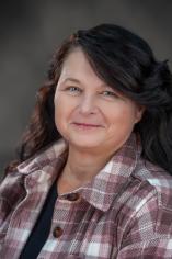 Portrait of Heidi Covan wearing a pink and white plaid jacket against a gray background.