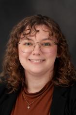 Headshot of Faye with curly brown hair and rounded glasses