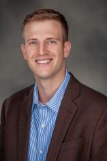 Asst. Professor Loren Hahn dressed professionally in a blue and white button up shirt under a dark blazer. 