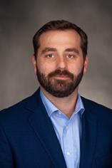 A man with dark hair and short beard in a blue suit and light blue shirt