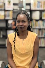Esther Popoola in a yellow shirt with a background of books on a shelf