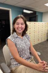 Student employee Hannah Kriedler sitting in a chair at the IRC desk. A cream filing cabinet and door are behind her.