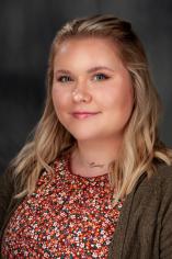 Picture of woman in red floral print top and green cardigan with a gray background
